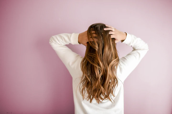Woman with long, healthy wavy hair against a soft pink background